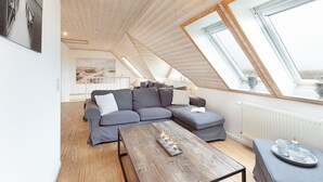 Un dormitorio tipo loft moderno con un tragaluz grande, techo de madera y una zona de estar acogedora con sofá y mesa de centro.