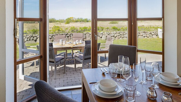 Un patio abierto con una mesa lista para comer, ventanas amplias y vistas del paisaje circundante.