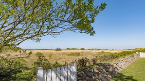 Una valla de madera blanca, un muro de piedra y un campo cubierto de hierba, con un árbol en primer plano.