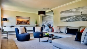 A modern living room with a sofa, armchairs, a coffee table, and a pendant light.