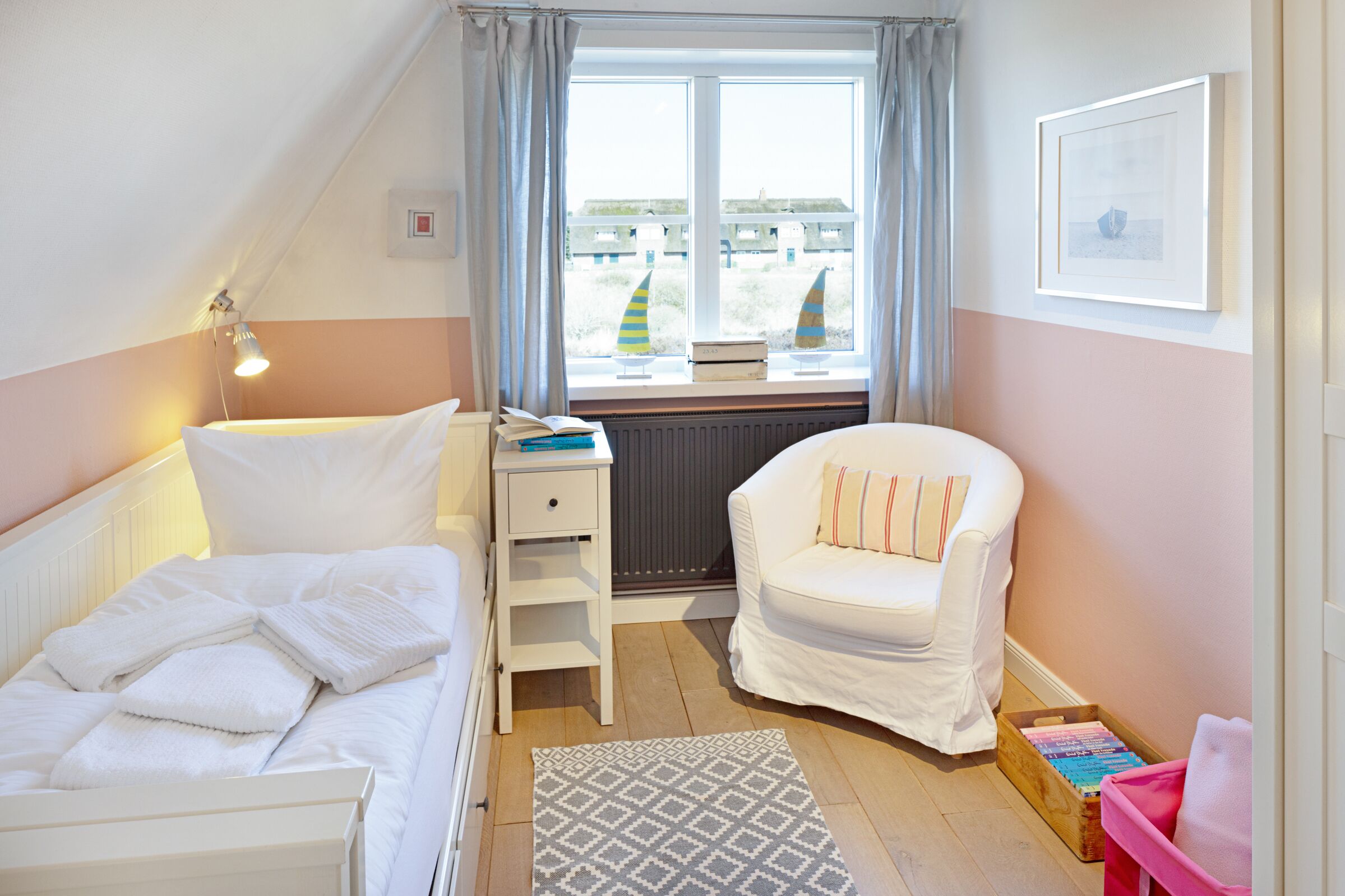 Een slaapkamer met een bed, een stoel, een bureau, een raam met gordijnen en een radiator.