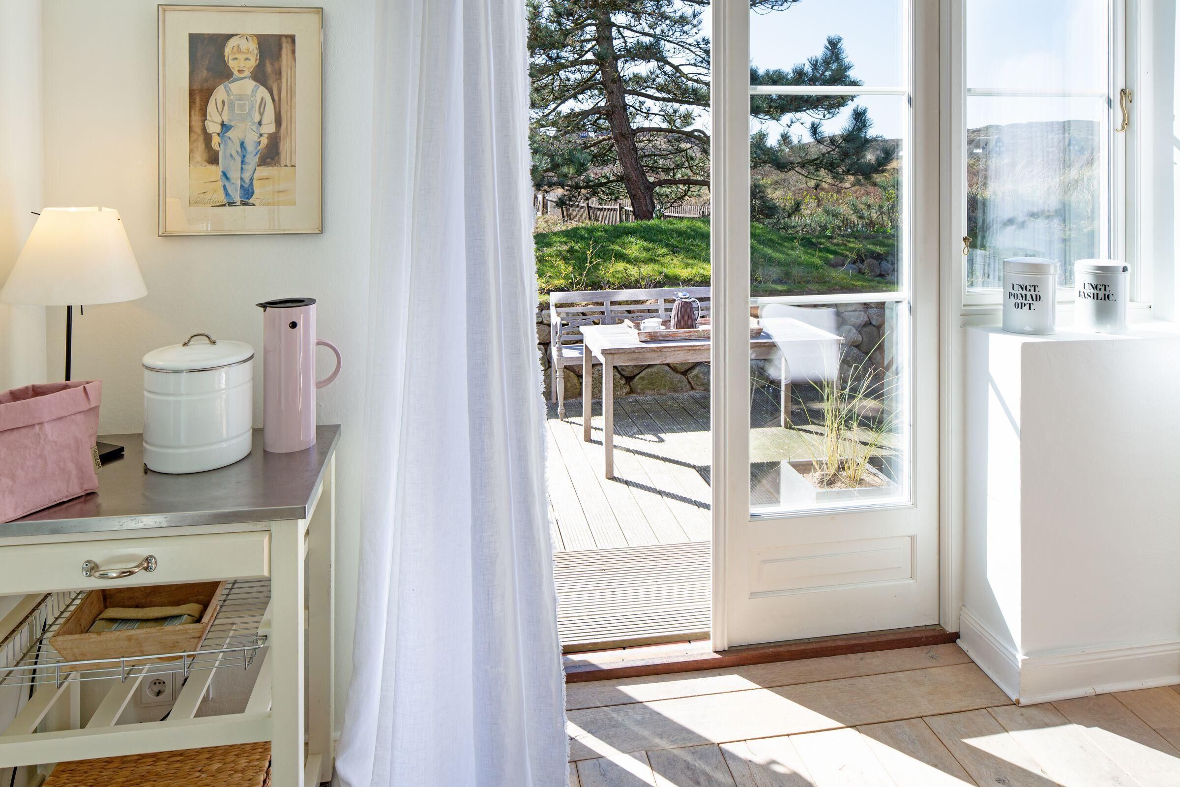 Ein Zimmer mit einer Schiebeglastür, die auf eine Terrasse mit Tisch und Stühlen führt, einem weißen Schrank zur Aufbewahrung und einem gerahmten Bild an der Wand.