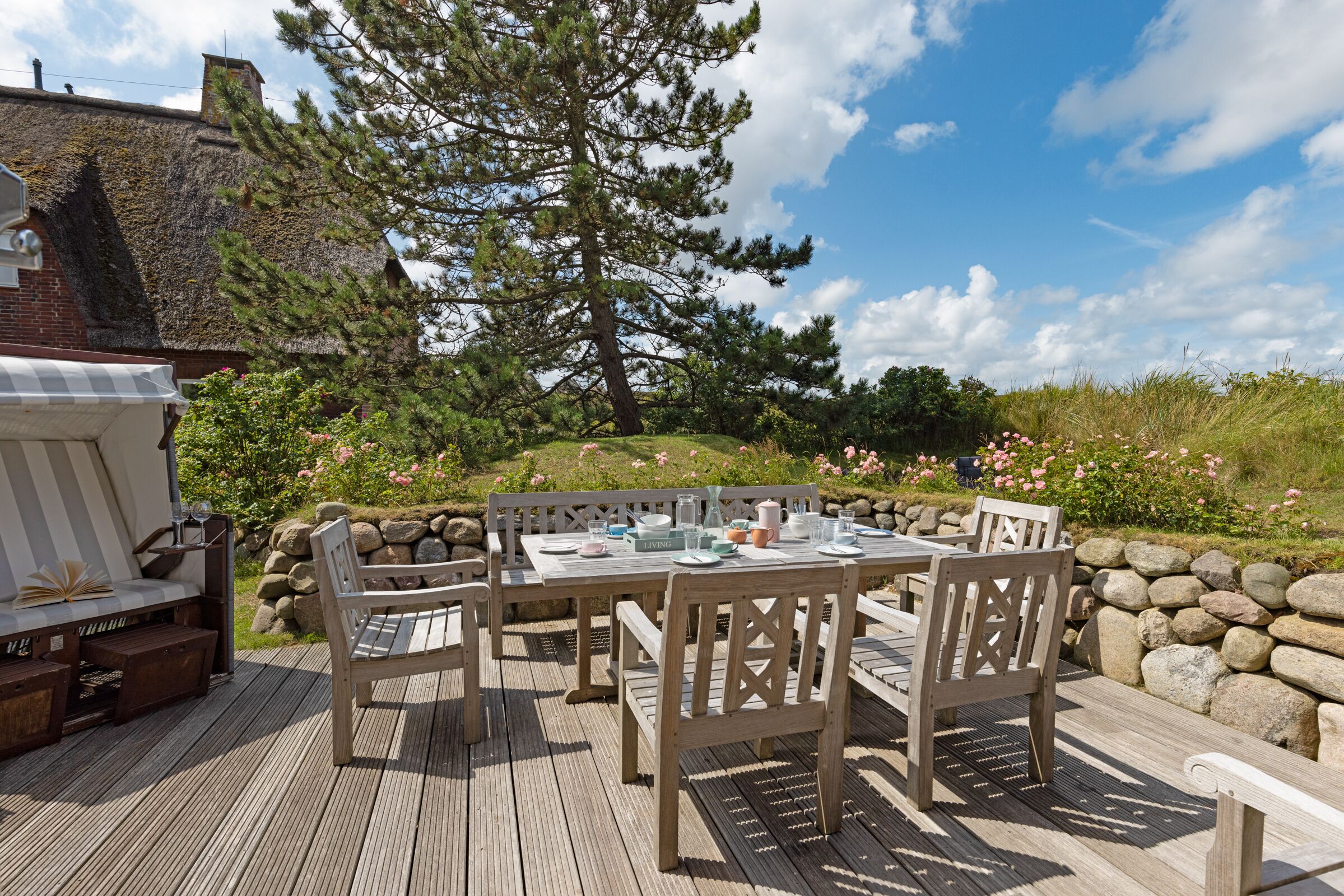 An outdoor dining area with a wooden deck, a table set for four, and a large tree in the background.