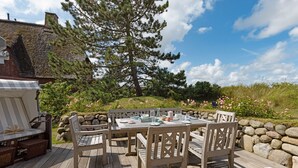 An outdoor dining area with a wooden deck, a table set for four, and a large tree in the background.
