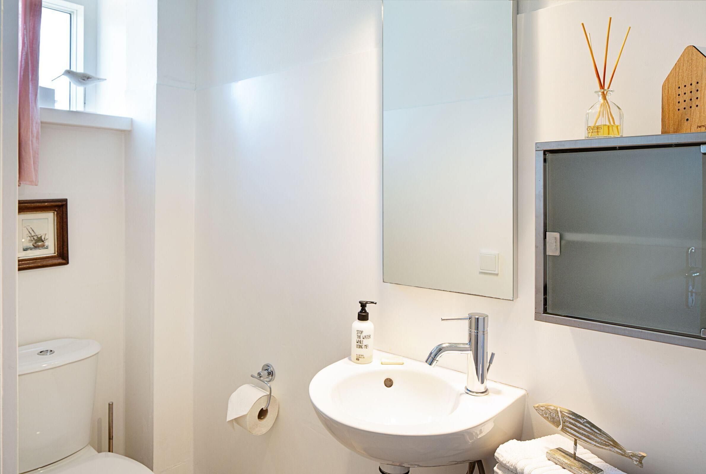 Une salle de bain avec un lavabo blanc, un miroir, des toilettes et un tableau encadré au mur.