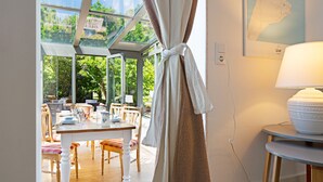Et spiseområde med et bord, stole, en lampe og udsigt gennem en glasdør.