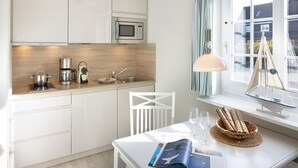 A modern kitchen with white cabinets, a microwave, a coffee maker, and a sink. There is a window with a view of houses and a sailboat model.