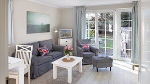 A modern living room with a grey sofa, white armchair, and ottoman, a small white table with a vase of flowers, and a television on a white cabinet.