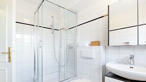 Ein modernes Badezimmer mit einer Duschkabine, einer weißen Toilette, einem Waschbecken mit zwei Gläsern und einem Spiegel darüber.
