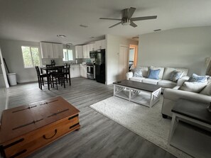 Ein modernes Wohnzimmer mit einem weißen Sofa, einem Holztisch und einer Essecke mit Tisch und Stühlen.