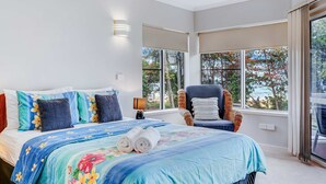 Un dormitorio con una cama, una silla, una lámpara y ventanas amplias.