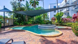 Una piscina con hidromasaje, rodeada de un patio de ladrillo y abundante vegetación.