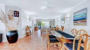 Un comedor amplio con una larga mesa y sillas de mimbre, un jarrón grande con plantas secas y obras de arte en las paredes.