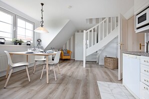 A modern kitchen with white cabinetry, a wooden dining table, and a staircase leading to an upper level. - Herzlich Willkommen im Appartement Hafenblick (List)