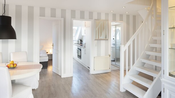 Un interior moderno con una escalera, una zona de comedor con mesa y sillas, y una cocina al fondo.