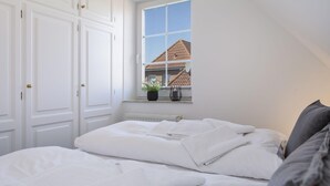 Un dormitorio con una cama bien hecha, una ventana con vista a una casa y puertas blancas.