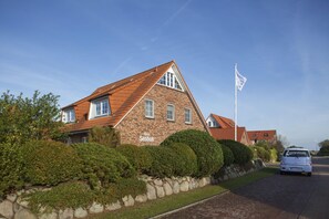 A charming two-story home with a pitched roof, surrounded by well-maintained hedges and a driveway.