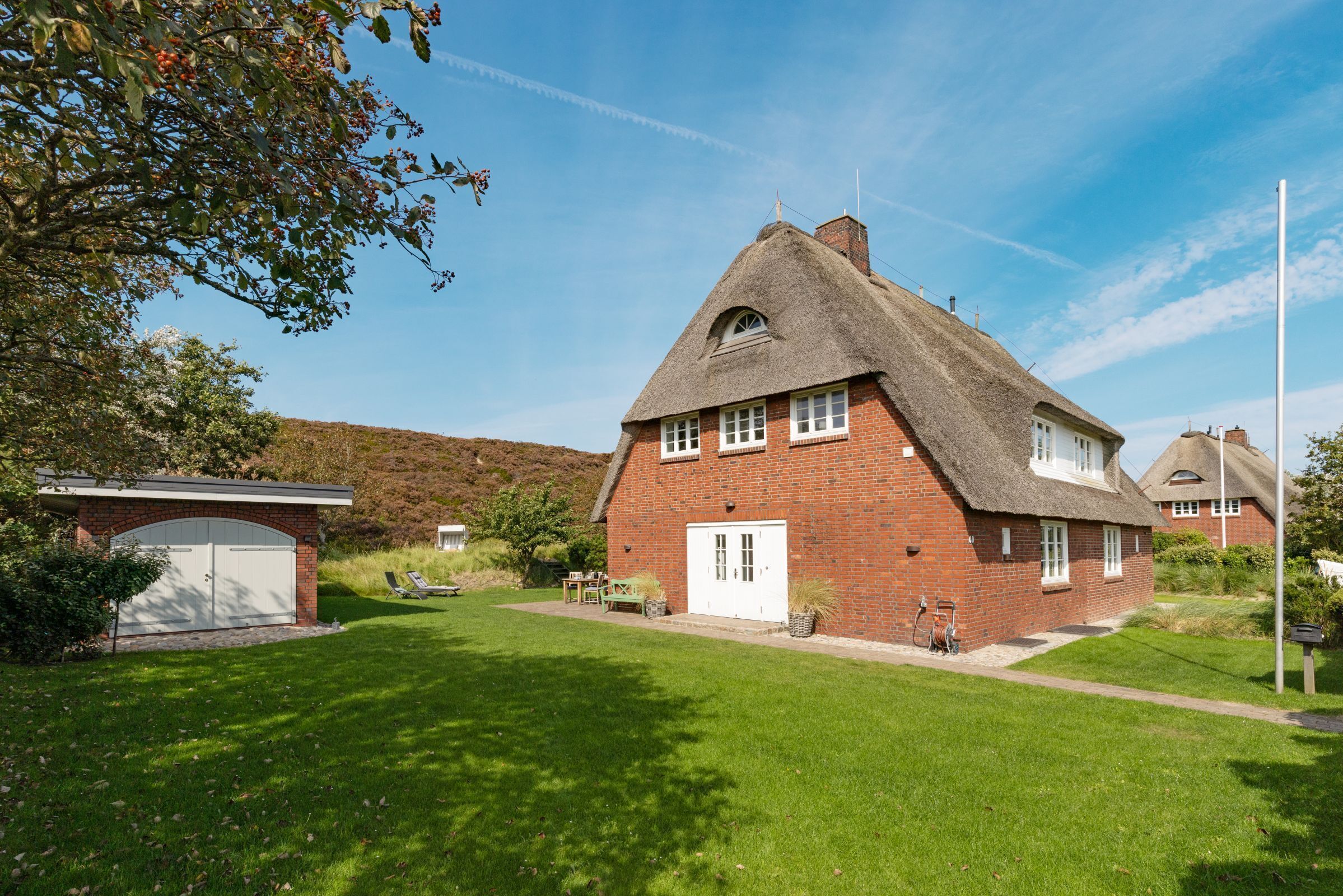 Une maison en briques avec un toit de chaume, un garage blanc et une pelouse bien entretenue.