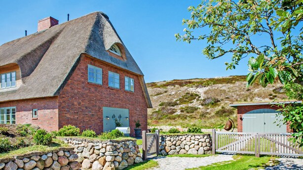 Una casa de ladrillo con un tejado pronunciado, un muro de piedra y un portón de madera.