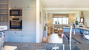 Una cocina moderna con electrodomésticos integrados, un comedor con sofá y mesa, y vistas a una sala de estar con chimenea.