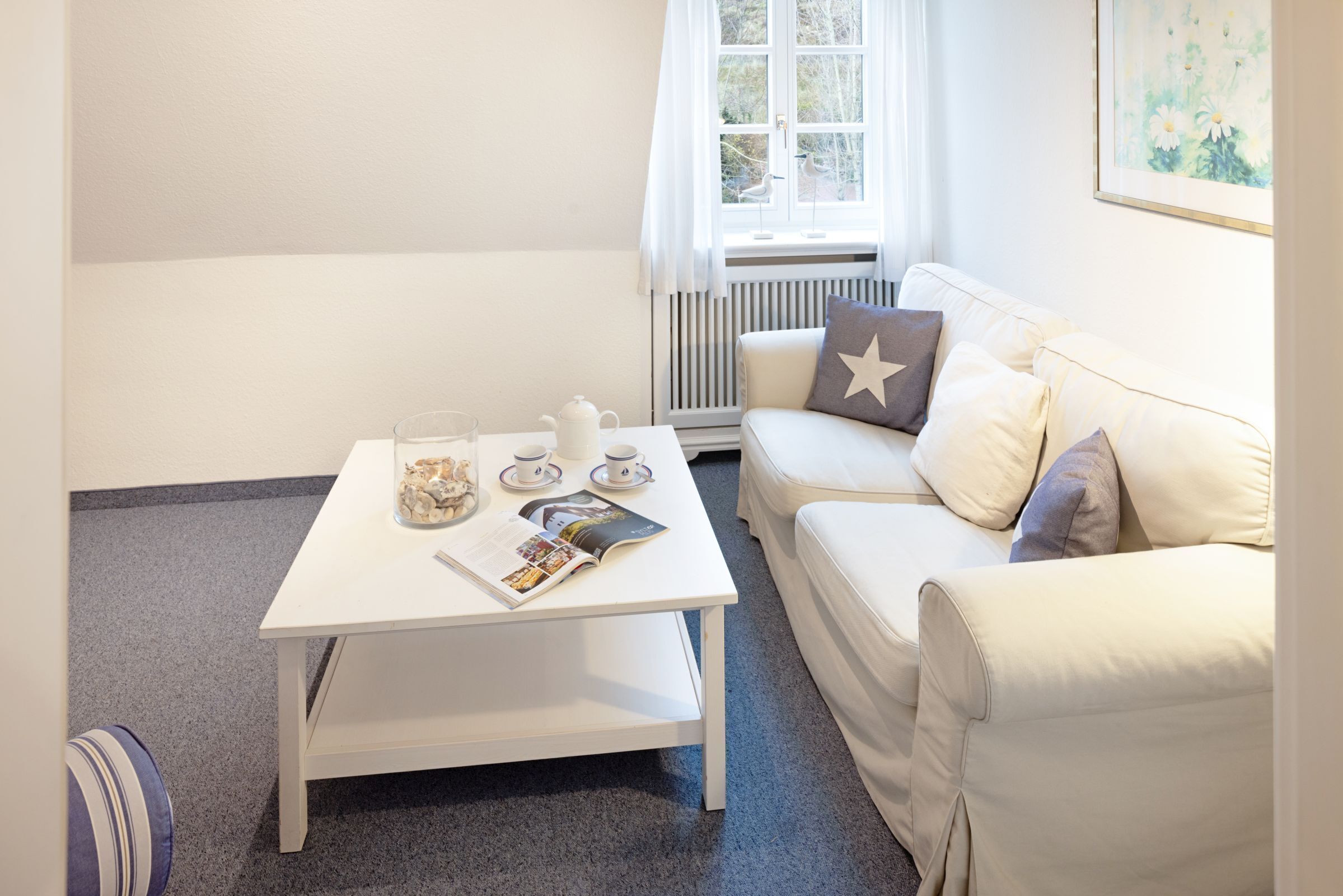 Ein modernes Wohnzimmer mit einem weißen Sofa, einem weißen Couchtisch und einem Fenster mit Vorhängen.