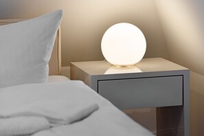 A neatly made bed with a white pillow and a bedside table with a round, illuminated light fixture. - Herzlich Willkommen im Ferienhaus Lotte (List)