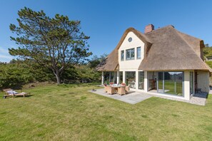 A house with a thatched roof, a patio with outdoor furniture, and a large tree in the background. - Herzlich Willkommen im Ferienhaus Lotte (List)