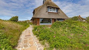 Ein Haus mit einem strohgedeckten Dach und einem steinernen Weg zum Eingang.