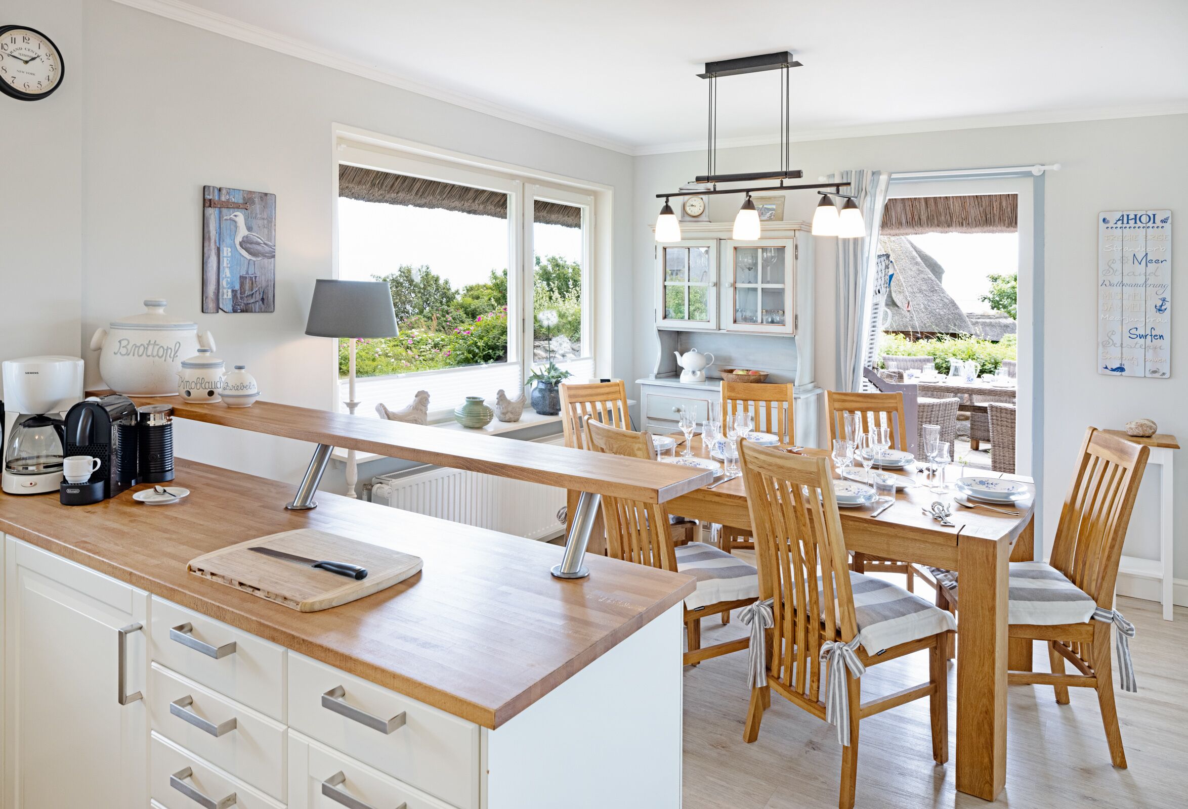 Una cocina luminosa con encimeras de madera, un comedor con mesa para cuatro, y vistas al jardín a través de grandes ventanales.