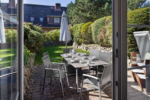 Une terrasse extérieure avec une table dressée pour quatre personnes, entourée de chaises et surmontée d’un grand parasol.