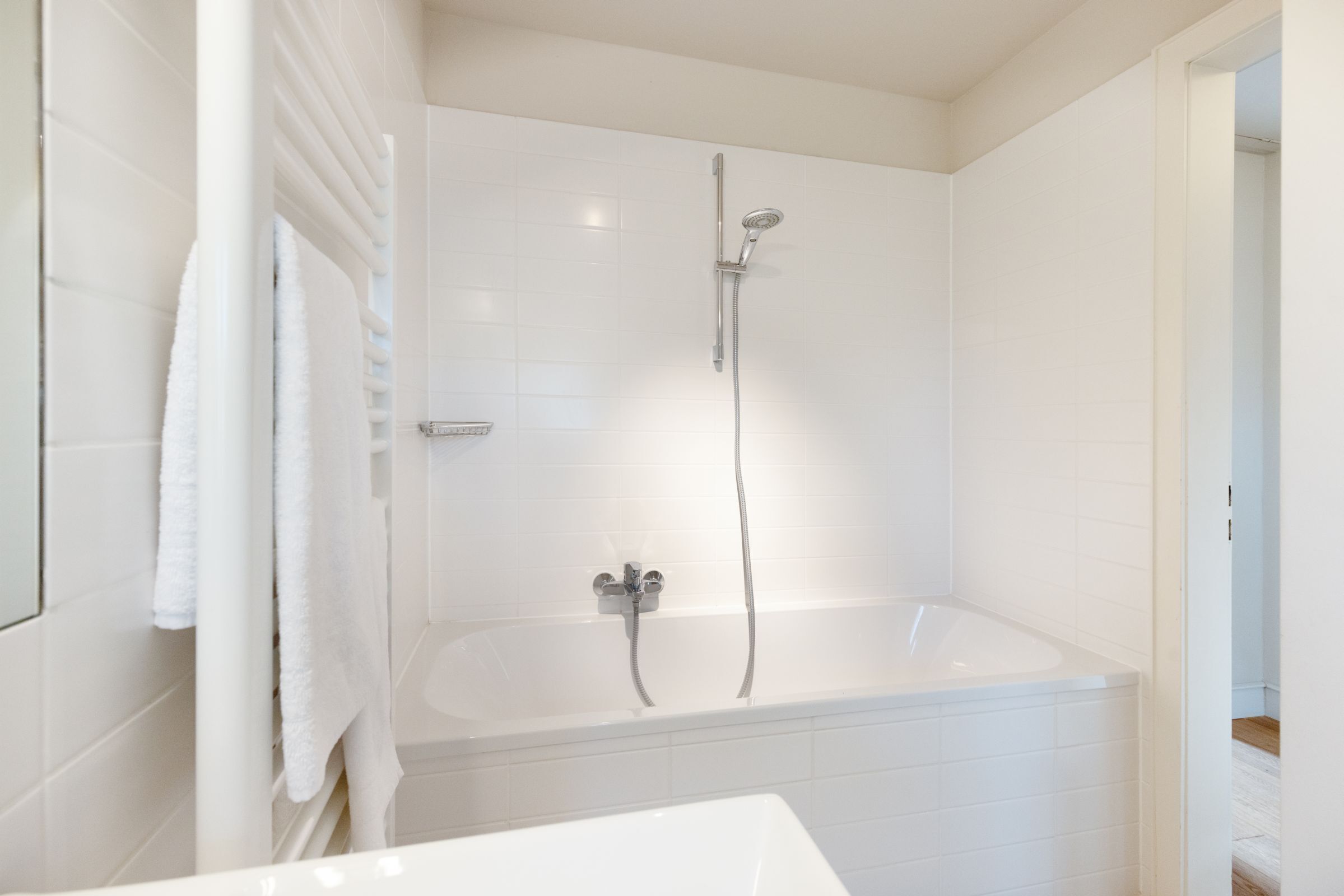 A modern bathroom with a white bathtub, a showerhead, and a towel rack.