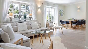 A spacious living room with a large sofa, a glass coffee table, and a dining area with a wooden table and chairs.