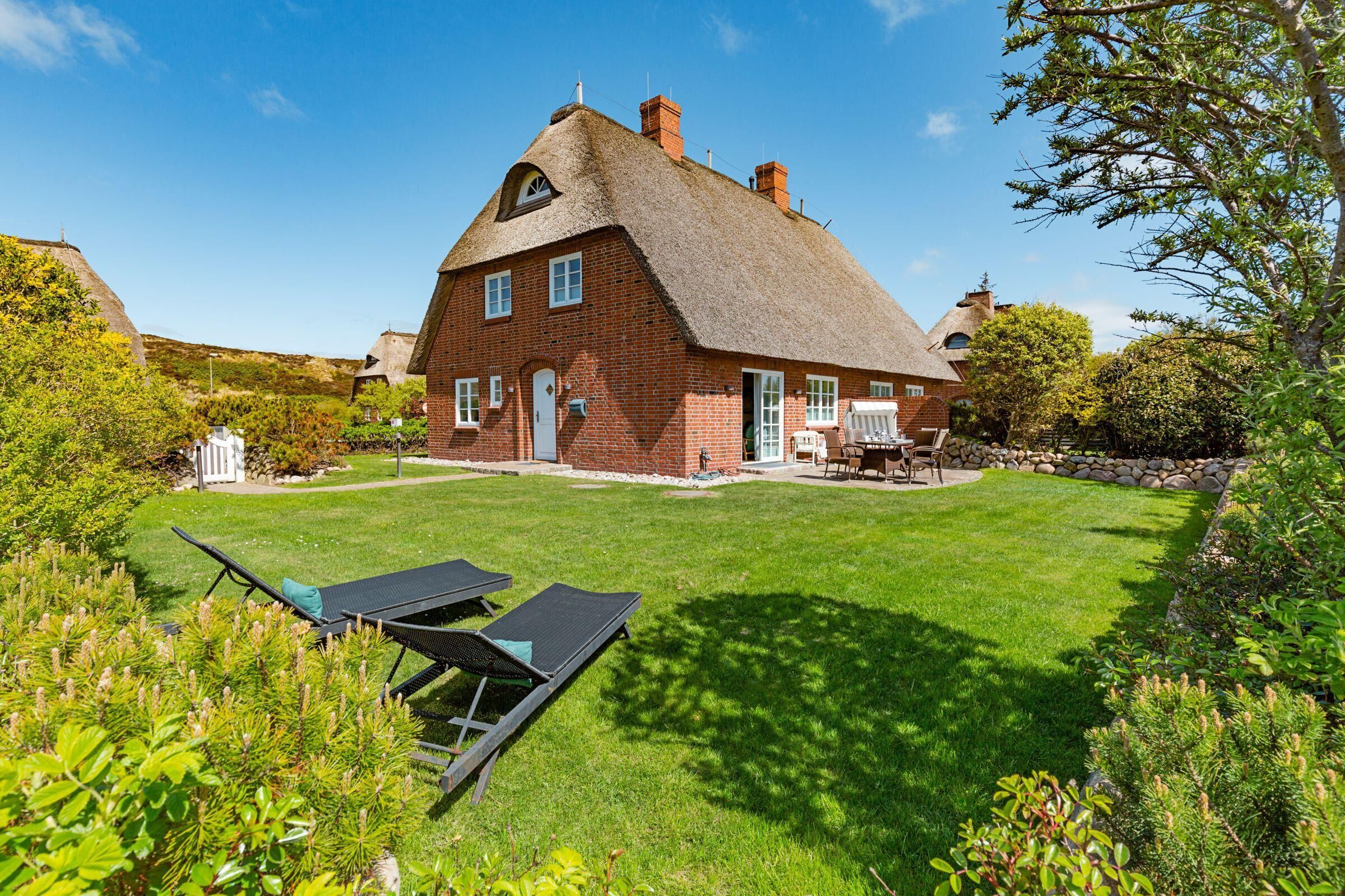 A large brick house with a thatched roof, a well-maintained lawn, and outdoor seating.