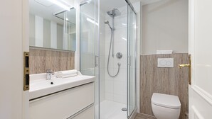 Une salle de bain moderne avec une douche à parois de verre, un lavabo blanc doté d’un plan de toilette en marbre et des toilettes blanches.