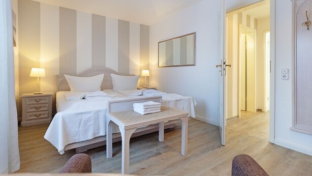 Une chambre d’hôtel avec un lit, des tables de chevet, une petite table avec des serviettes et un miroir au mur.