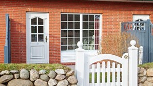 Une maison en briques rouges avec une porte et des fenêtres blanches, une clôture en bois peinte en blanc et un mur en pierre.