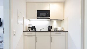 Une cuisine compacte avec des meubles blancs, un micro-ondes noir, une machine à café et une bouilloire.