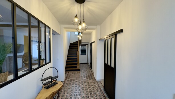 Un pasillo con baldosas de diseño, un banco de madera, un aplique colgante y una escalera al fondo.