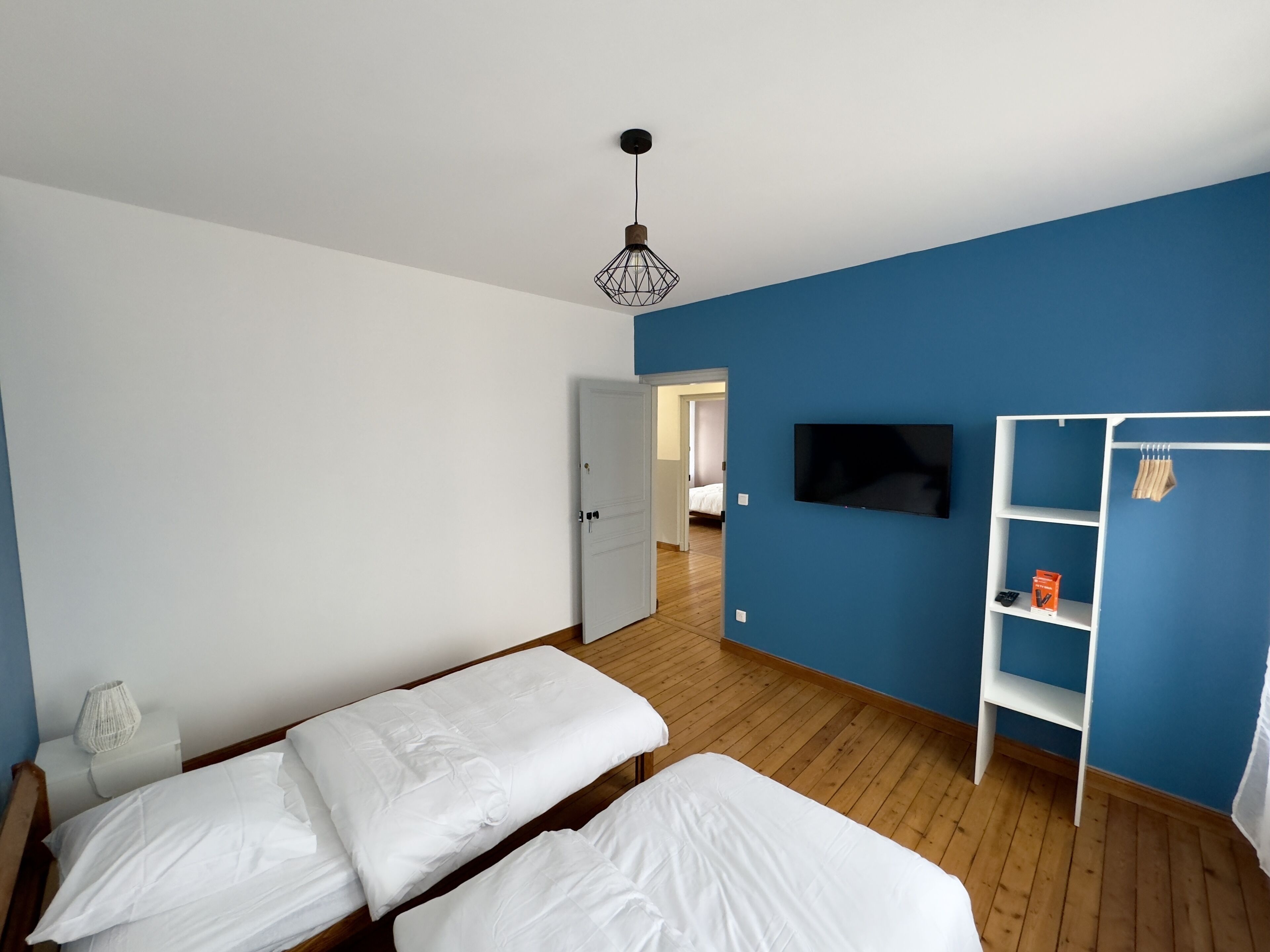 A bedroom with two beds, a TV, a wardrobe, and a wooden floor.
