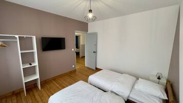 A bedroom with a wooden floor, a TV mounted on the wall, a wardrobe, and a bed with white bedding.