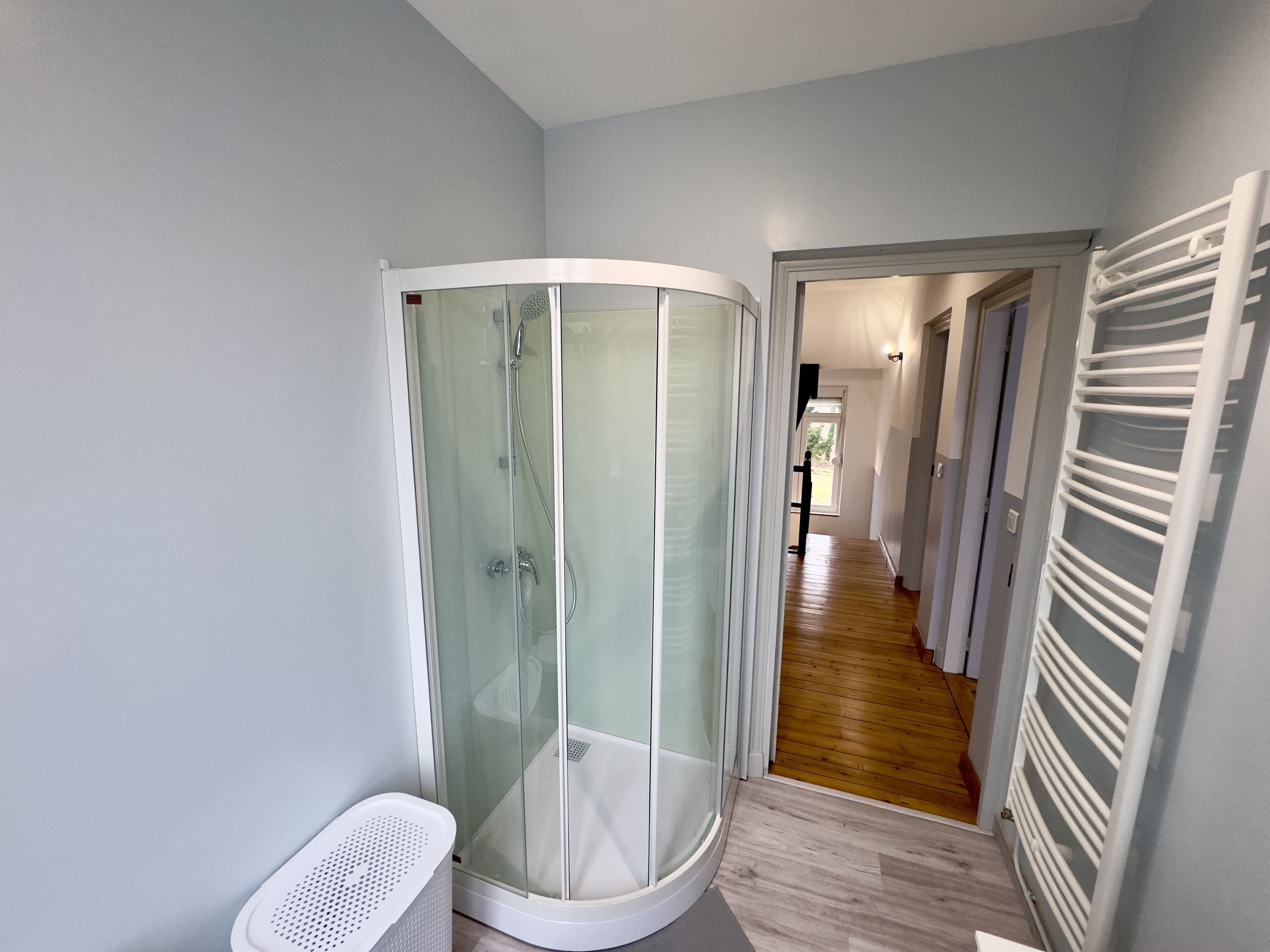 Un bagno moderno con box doccia in vetro, portasciùgli mani bianco e pavimento in legno.