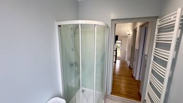 Un bagno moderno con box doccia in vetro, portasciùgli mani bianco e pavimento in legno.