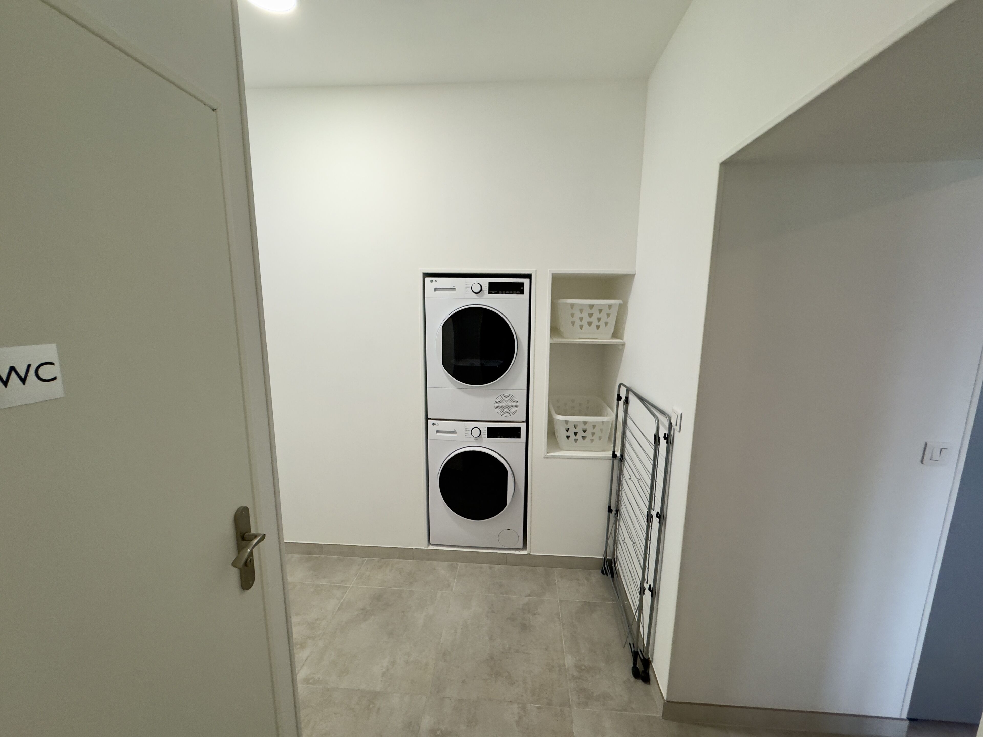 A laundry room with two stacked washing machines, a drying rack, and storage shelves.