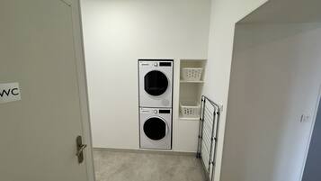 A laundry room with two stacked washing machines, a drying rack, and storage shelves.