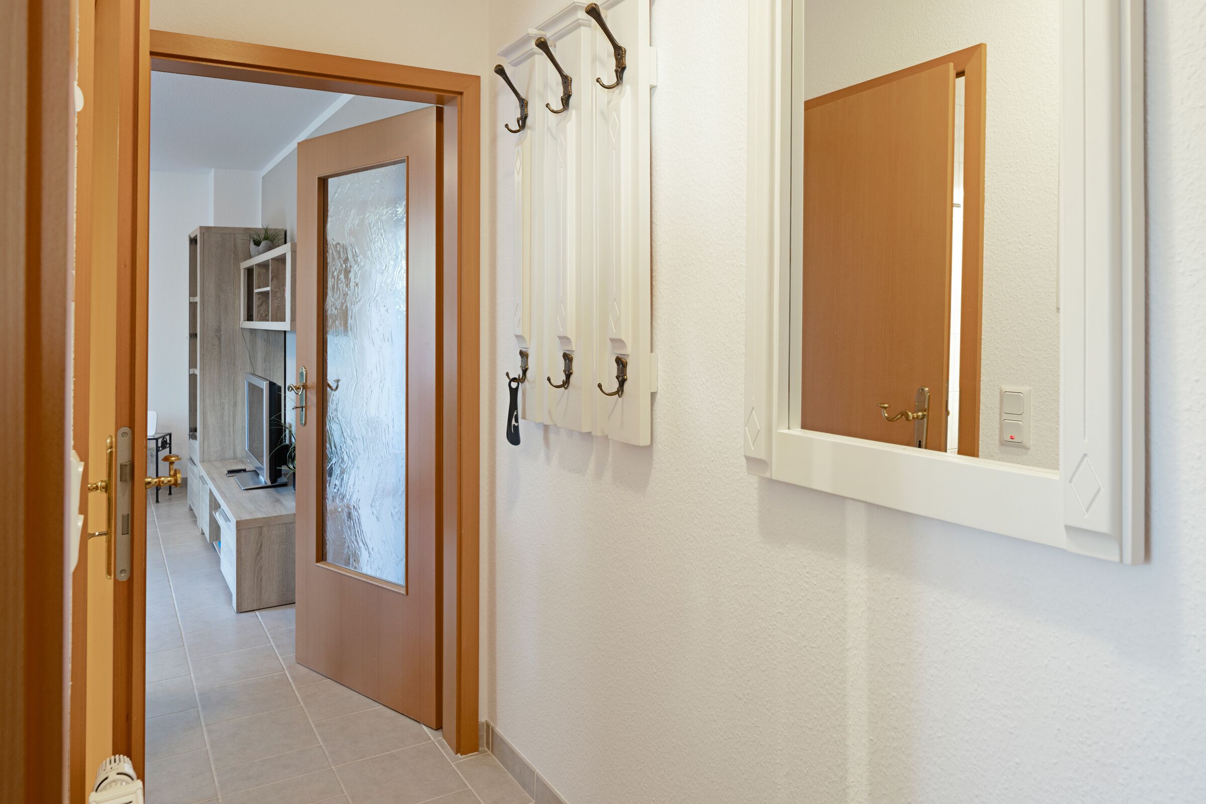 Un pasillo con una puerta de madera, un perchero y un espejo en la pared.