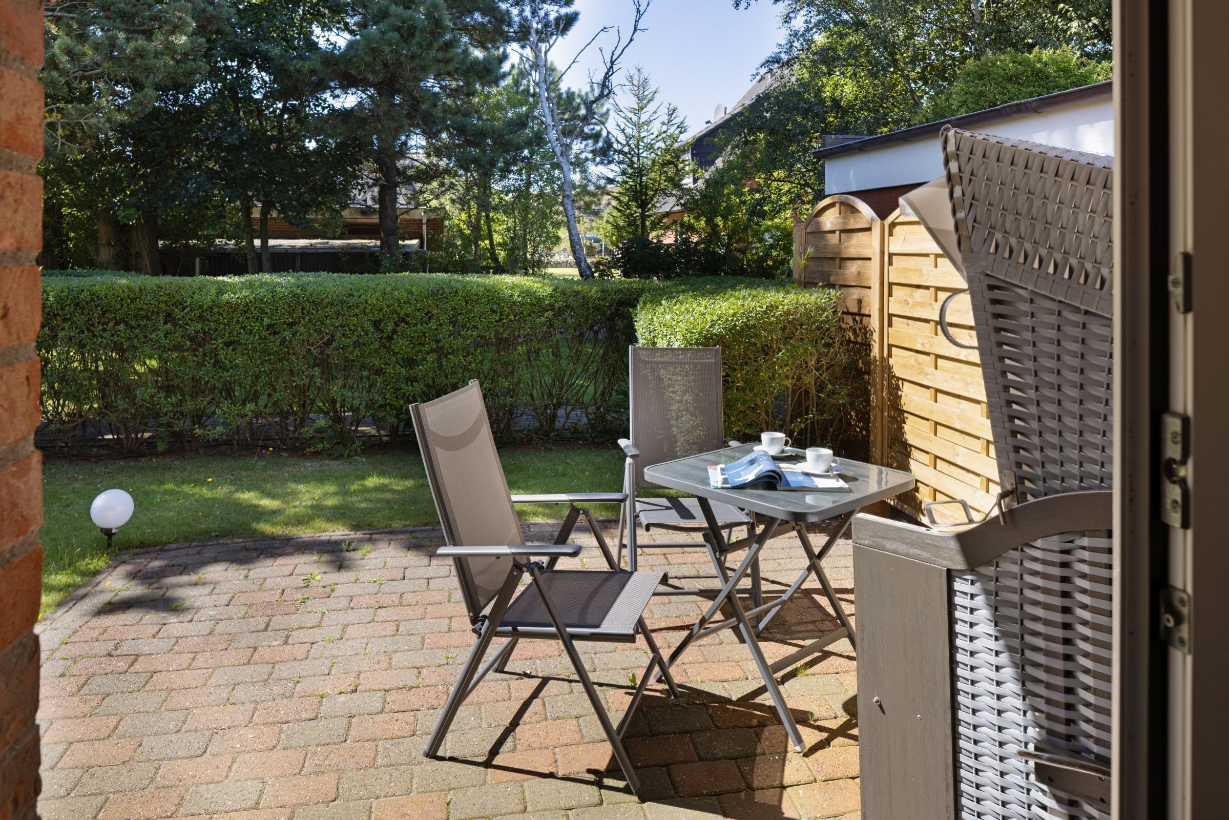 An outdoor patio with a table and chairs, a brick floor, and a wooden fence.