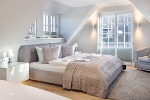 Ein Schlafzimmer mit einem Bett, Nachttischen, einer Lampe, einem Sessel und einem großen Fenster mit Jalousien.