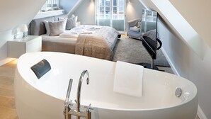 Une chambre à coucher moderne avec une grande baignoire sur pieds, un lit soigneusement fait et une fenêtre équipée de stores.