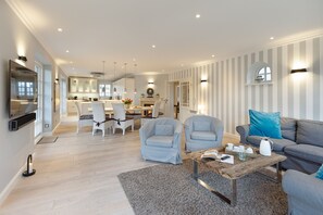 A modern living room with a grey sofa, two armchairs, a coffee table, and a dining area with a chandelier.