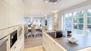 Une cuisine moderne avec des meubles blancs, un îlot central et de grandes fenêtres donnant sur l’extérieur.